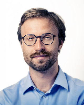 Man wearing glasses and a light blue shirt against a white background
