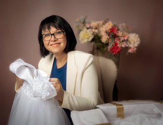 Business-woman and community supporter with short black hair and glasses holds a a white lace and tulle wedding dress donated as a special gift for a child.