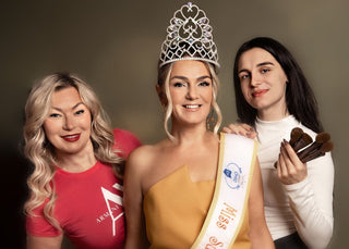 Three women, one wearing a beauty pageant crown and sash, against a plain background.