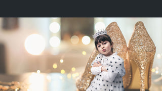 Child in a polka dot dress with a tiara and large gold shoes against a blurred light background