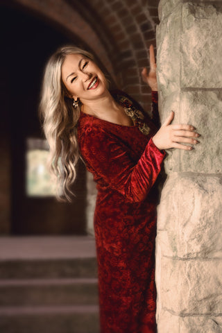 Woman in a red dress leaning against a stone wall in an archway.