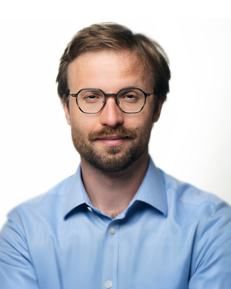Man wearing glasses and a light blue shirt against a white background