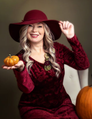 Woman in a red dress and hat holding a small pumpkin against a neutral background