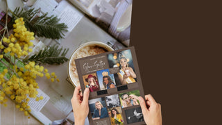 Person holding a photo album with multiple photos on a table with flowers and a cup.