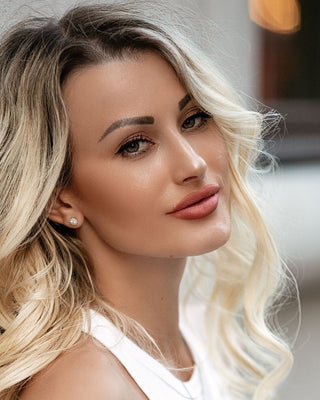 Close-up of a woman with blonde hair and a white top, blurred background