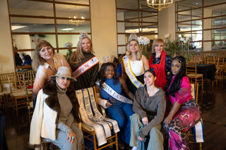 Five women with crowns and sashes in a room with chairs and tables.