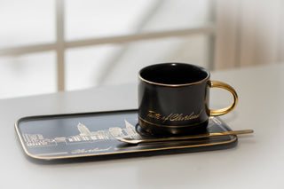 Black mug with gold interior on a matching tray on a white surface.