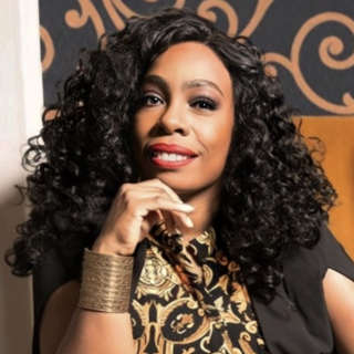 Woman with curly hair sitting in a decorative chair against a patterned wall.