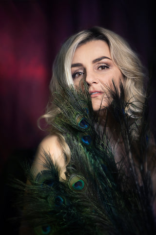 Woman with peacock feathers against a dark background