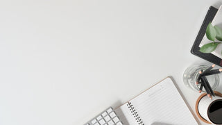 White desk with a notebook, keyboard, pen, and glass of water on a light gray background
