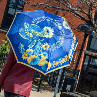 Beautiful young lady, showing her support and solidarity with Ukraine. Holding open   Holding open umbrella with symbolic ukrainian colors of Yellow - Blue featuring Ukrainian phoenix bird and yellow-blue sunflowers.